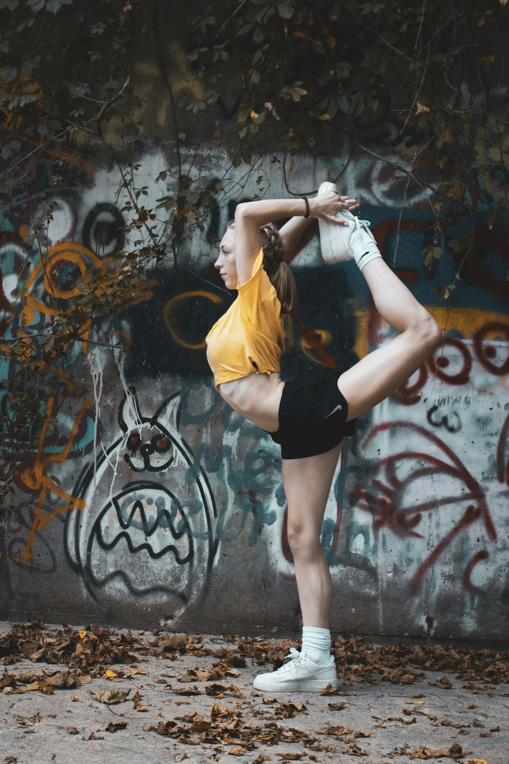woman in yellow shirt and black shorts standing near wall with graffiti