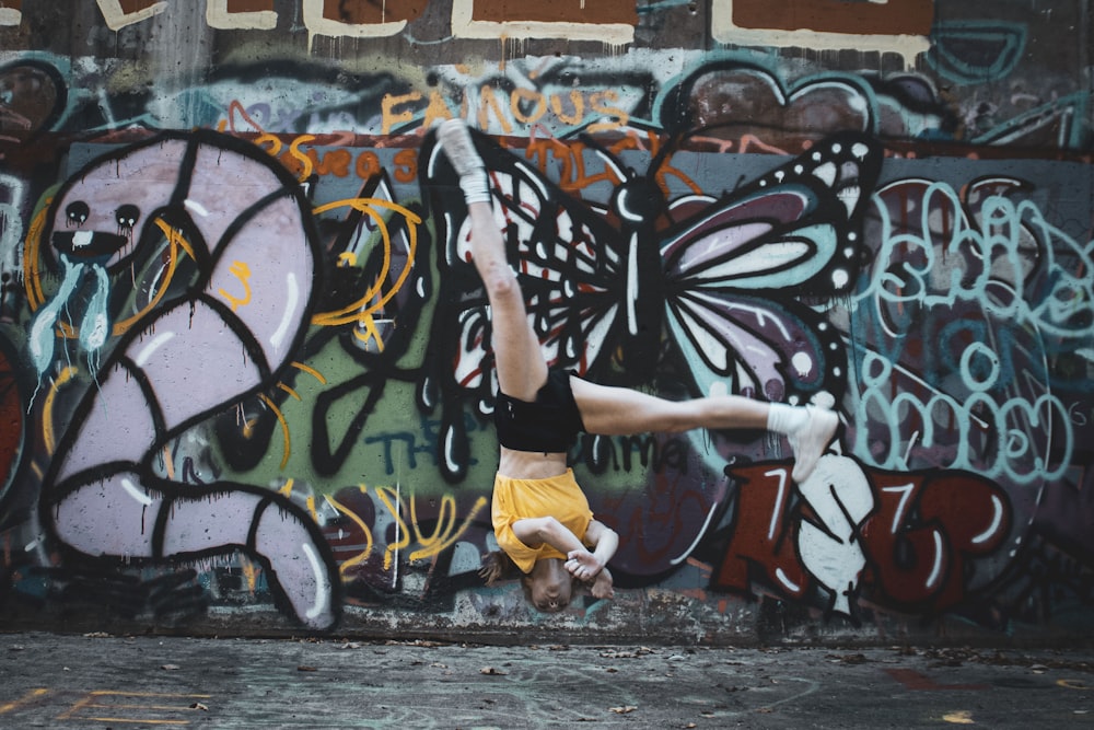 Mujer con camiseta sin mangas negra y pantalones cortos de mezclilla azul de pie junto a la pared de graffiti durante el día
