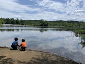 Children playing quietly on the soft sandy shoreline beside a peaceful lake.