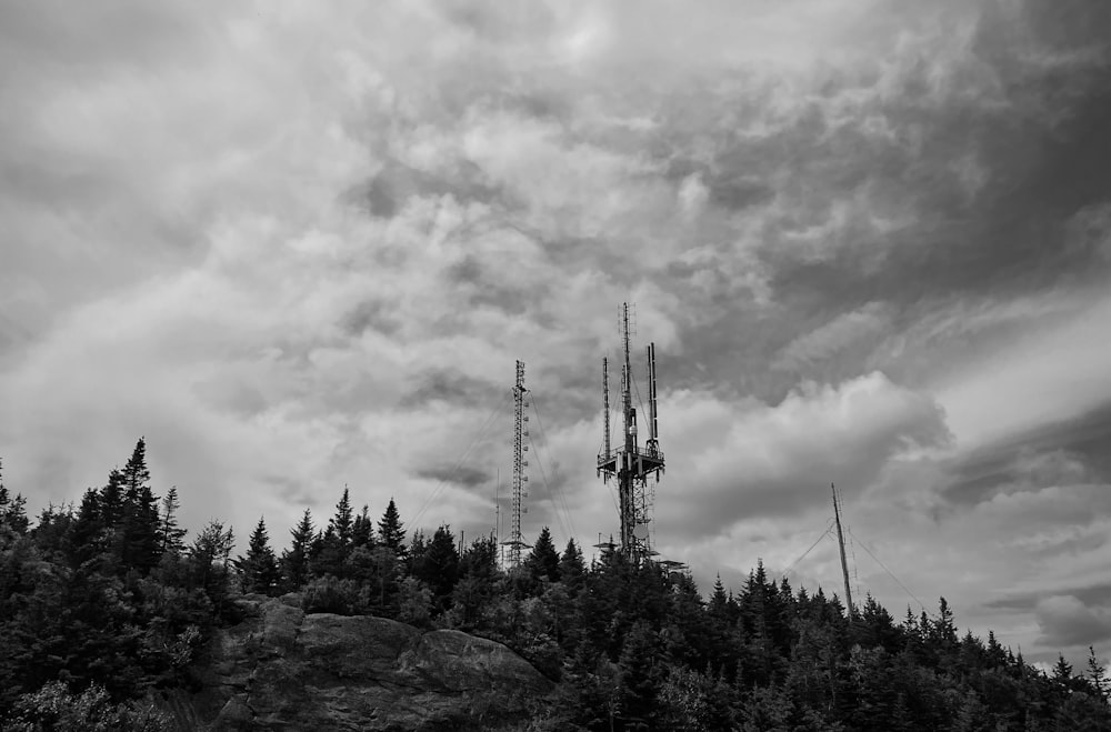 grayscale photo of trees and windmill under cloudy sky