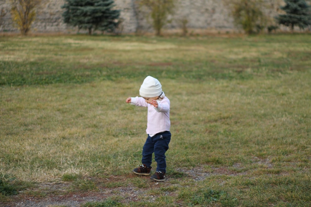 child in white hoodie and blue pants walking on green grass field during daytime