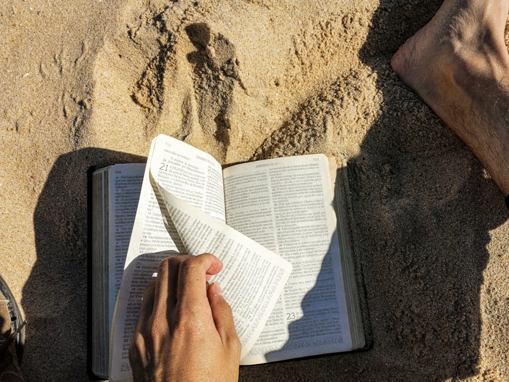 person reading book on brown sand during daytime