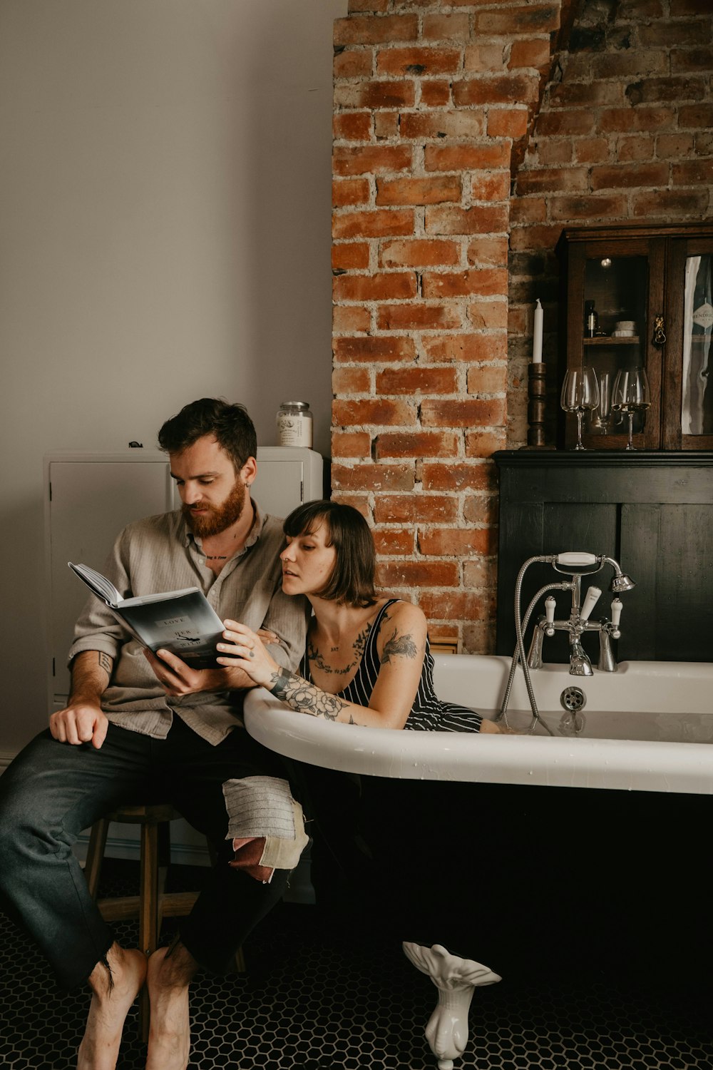 man and woman sitting on bathtub reading book