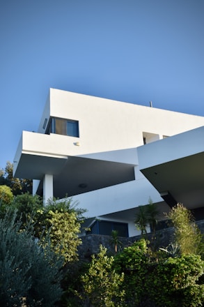 A sleek modern steel villa surrounded by lush greenery under a clear sky.