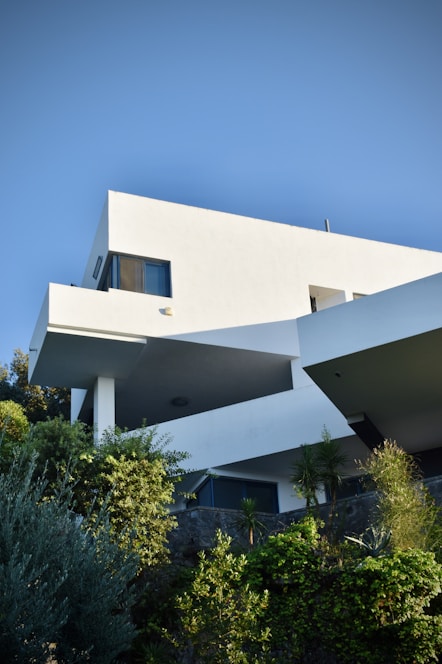 A modern bioclimatic house surrounded by lush greenery under a clear blue sky.