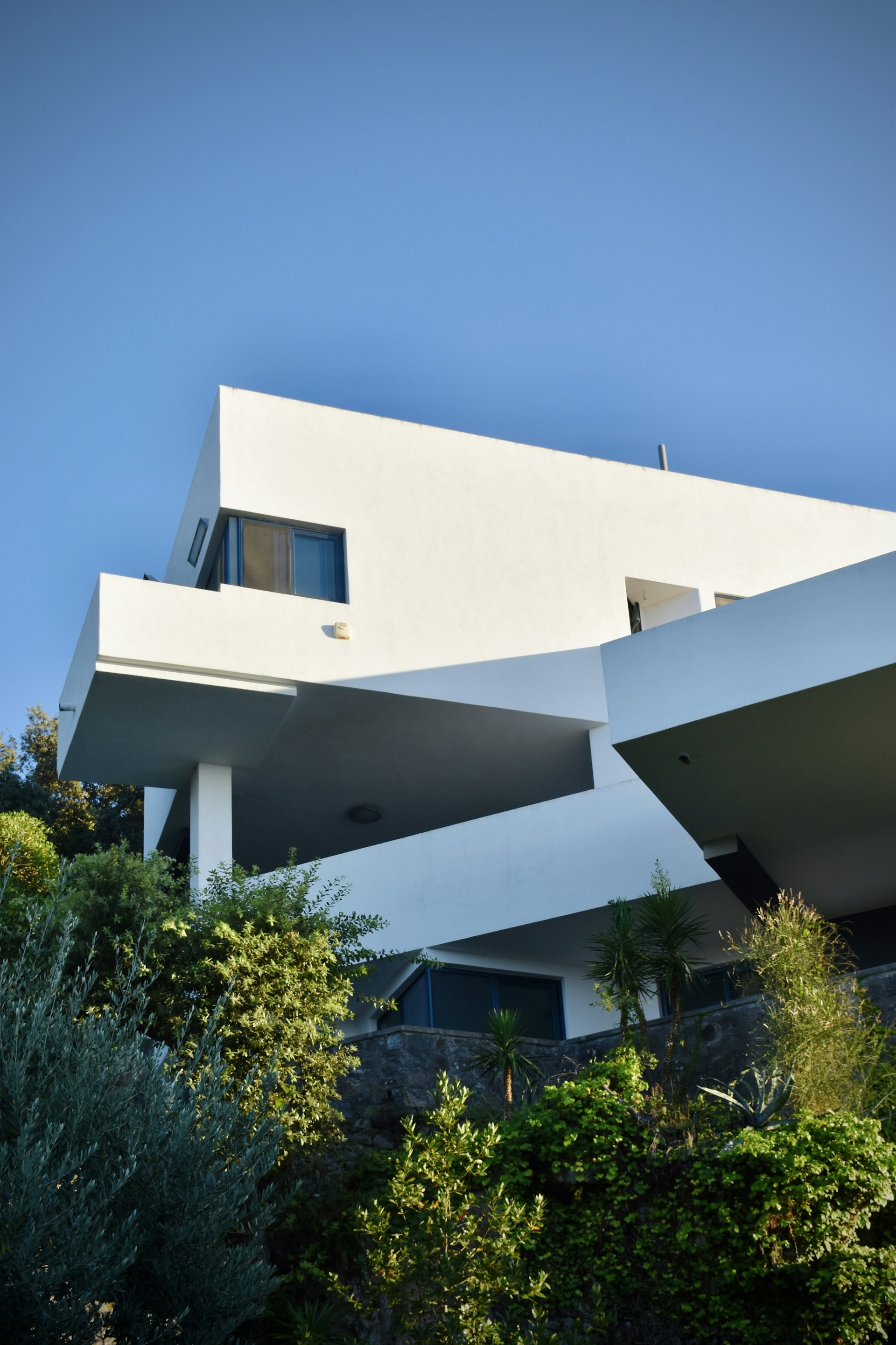 A modern container farmhouse surrounded by lush greenery under a clear blue sky.