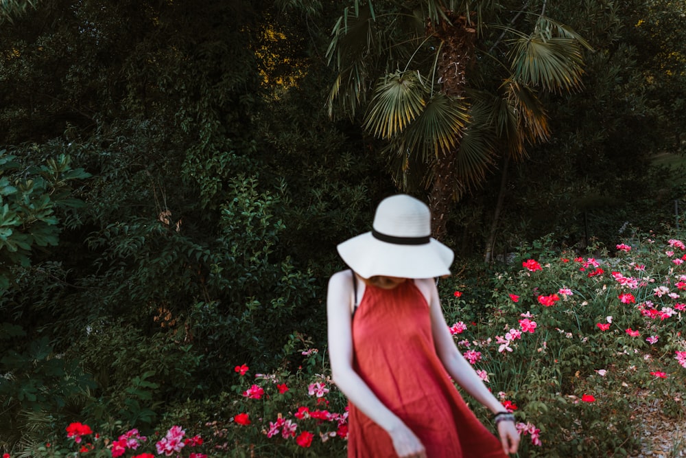 woman in red dress wearing white hat standing in front of green plants