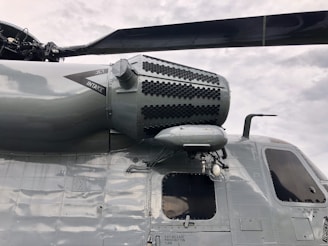 Close-up view of a helicopter's side featuring the jet intake and rotor assembly. The surface is made of smooth, polished metal, reflecting a grayish hue. The helicopter shows intricate details, including labeled components and a visible part of the rotor blade.