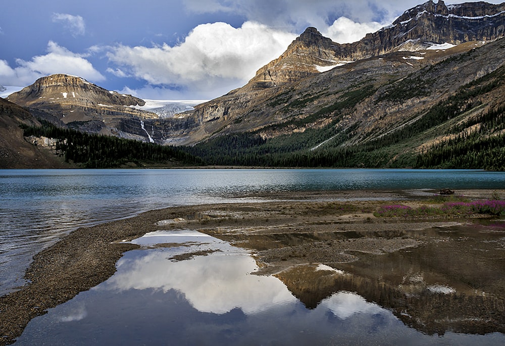 lake near green and brown mountains under white clouds and blue sky during daytime