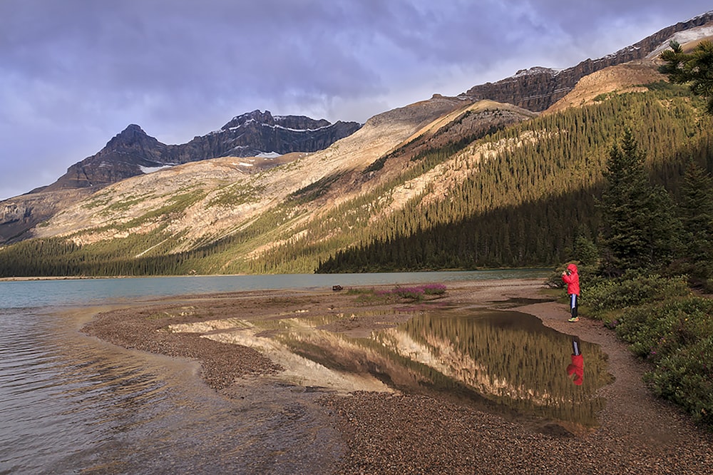 낮 동안 호수 근처의 갈색 모래 위에 서 있는 빨간 재킷을 입은 사람