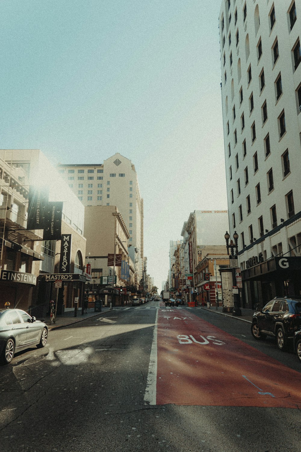 cars parked on side of the road in between high rise buildings during daytime