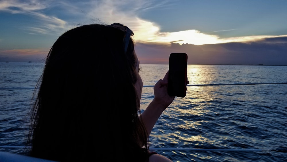 woman holding smartphone near body of water during daytime