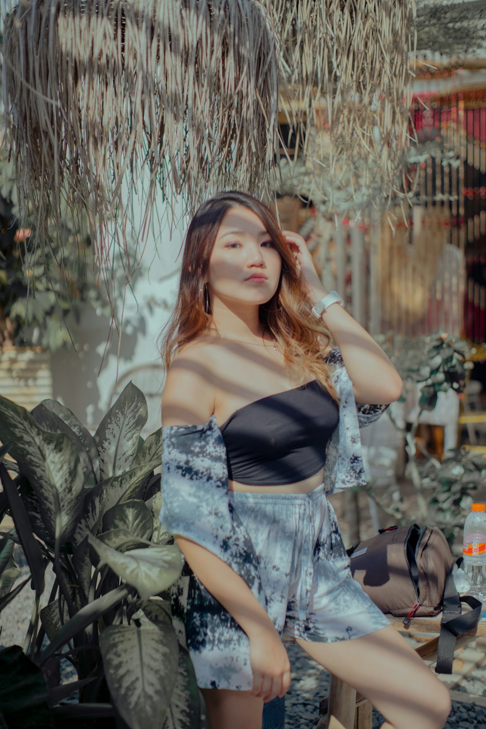 woman in black and white spaghetti strap top and blue denim shorts sitting on green plant