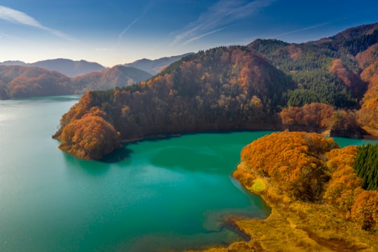 brown and green mountain beside blue lake under blue sky during daytime in Semboku Japan