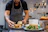 Chef demonstrating sandwich assembly with a group of attentive home cooks in a bright kitchen studio.