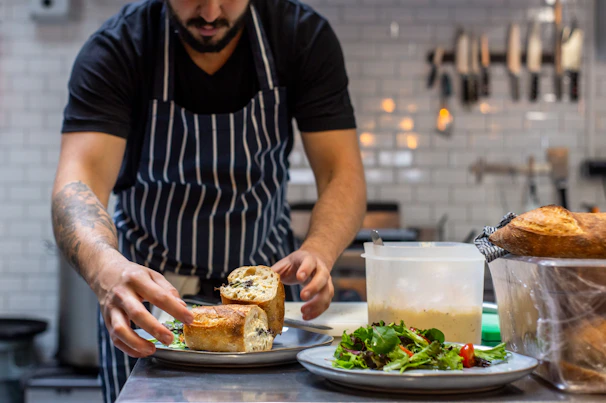 A chef demonstrating sandwich layering techniques to a small group in a cozy kitchen setting.