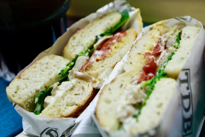 Hand holding a wrapped bagel sandwich filled with fresh greens and grilled chicken.