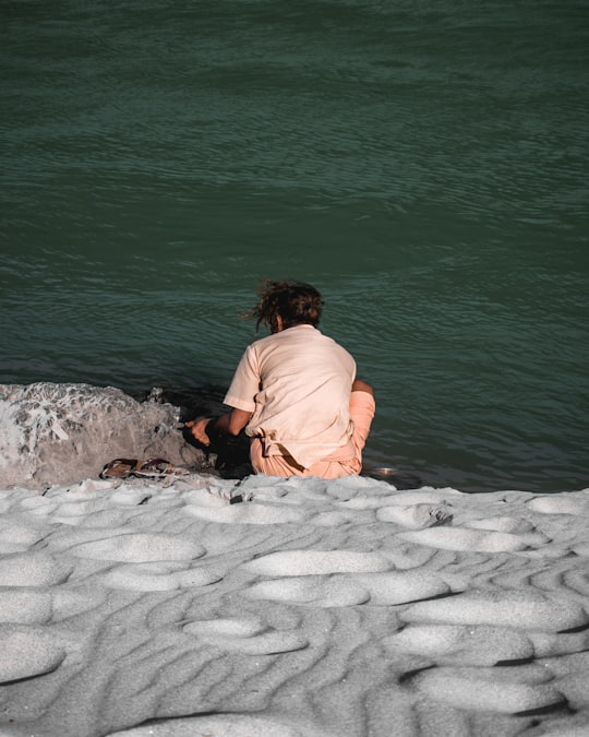 woman in brown shirt sitting on white sand near body of water during daytime in Rishikesh India