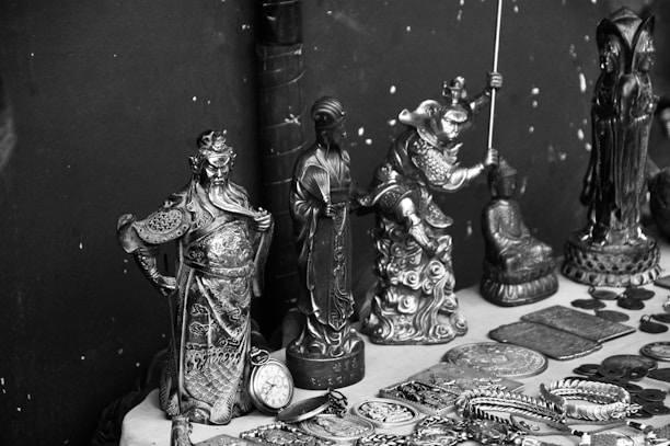 A collection of intricately designed metal figurines and objects displayed on a surface. The figurines depict various characters, some in dynamic poses, and are surrounded by several round coins and decorated plates. The items seem to be of cultural or historical significance and feature elaborate details in their craftsmanship.