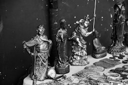 A collection of intricately designed metal figurines and objects displayed on a surface. The figurines depict various characters, some in dynamic poses, and are surrounded by several round coins and decorated plates. The items seem to be of cultural or historical significance and feature elaborate details in their craftsmanship.