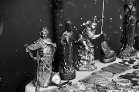 A collection of intricately designed metal figurines and objects displayed on a surface. The figurines depict various characters, some in dynamic poses, and are surrounded by several round coins and decorated plates. The items seem to be of cultural or historical significance and feature elaborate details in their craftsmanship.