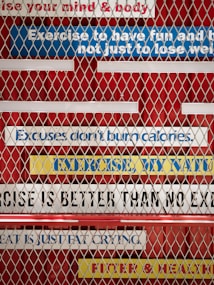A metal fence with motivational fitness quotes written on colorful strips of tape in the background. The phrases include 'Exercise to have fun and be fit, not just to lose weight,' 'Excuses don't burn calories,' 'No exercise is better than no exercise,' 'Sweat is just fat crying,' and 'Fitter & healthier.' The strips are mostly white, blue, and yellow, placed on a red background.