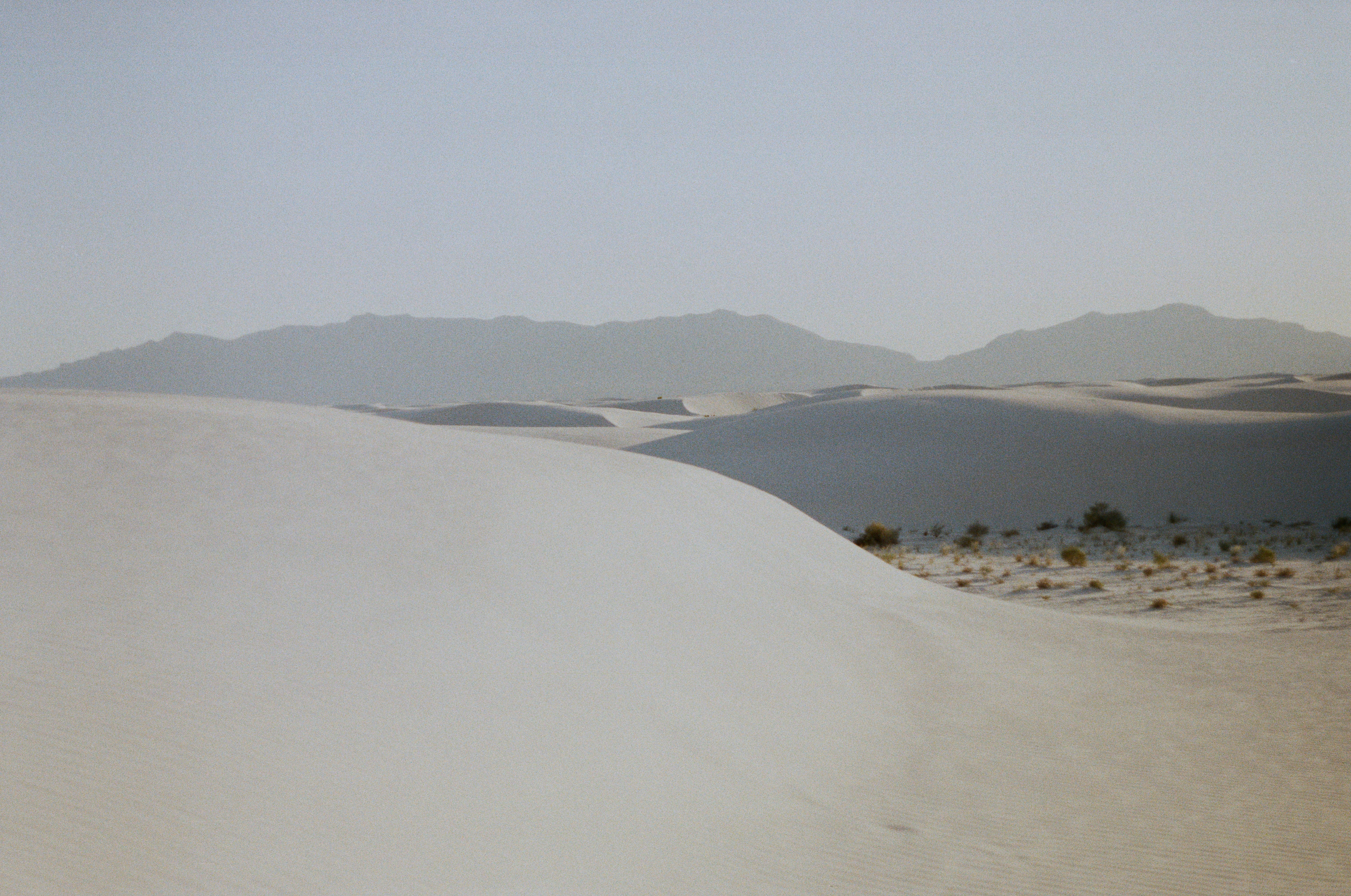 white sand with green grass and mountains in the distance, 