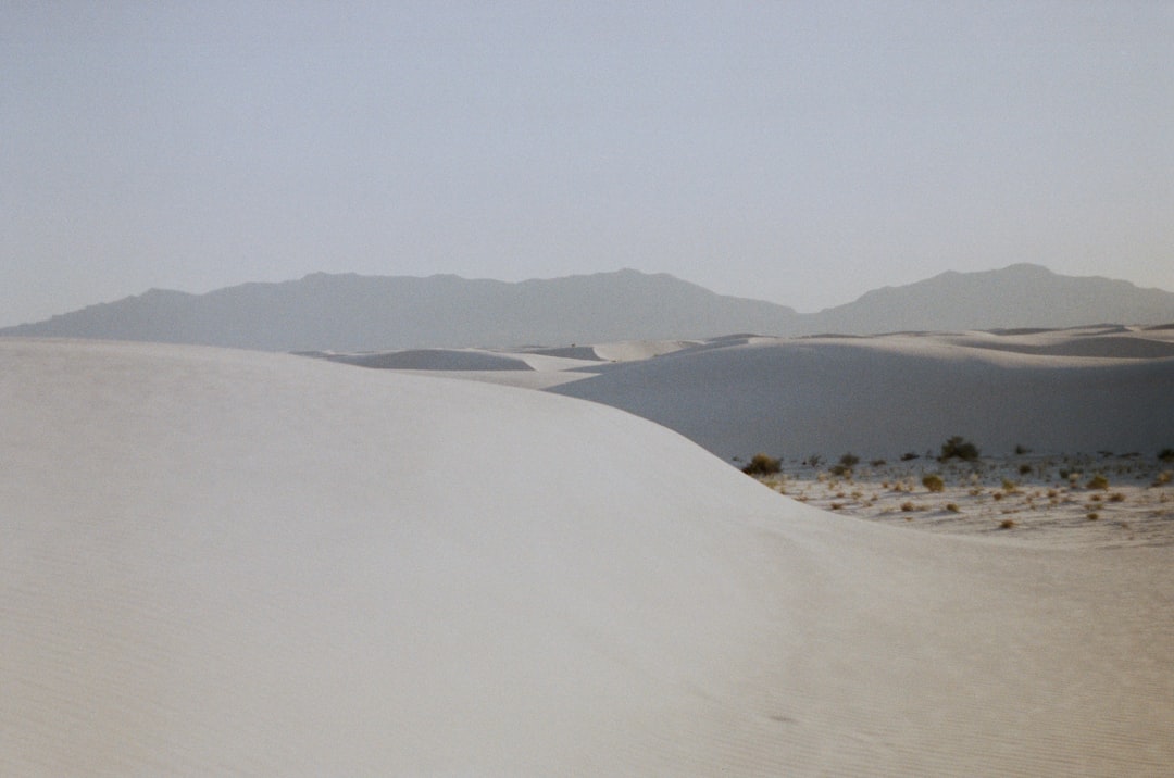 white sand with green grass and mountains in the distance,