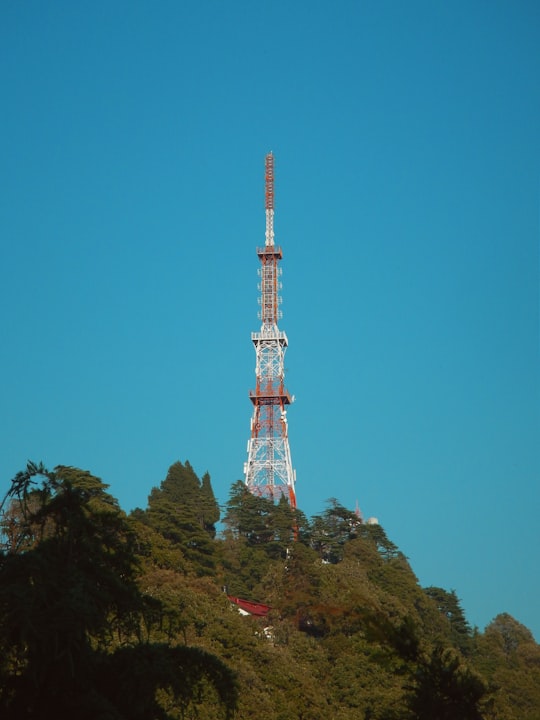 white and red tower surrounded by trees under blue sky during daytime in Mussoorie India