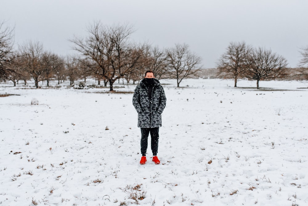 mulher em casaco preto e branco andando no chão coberto de neve durante o dia
