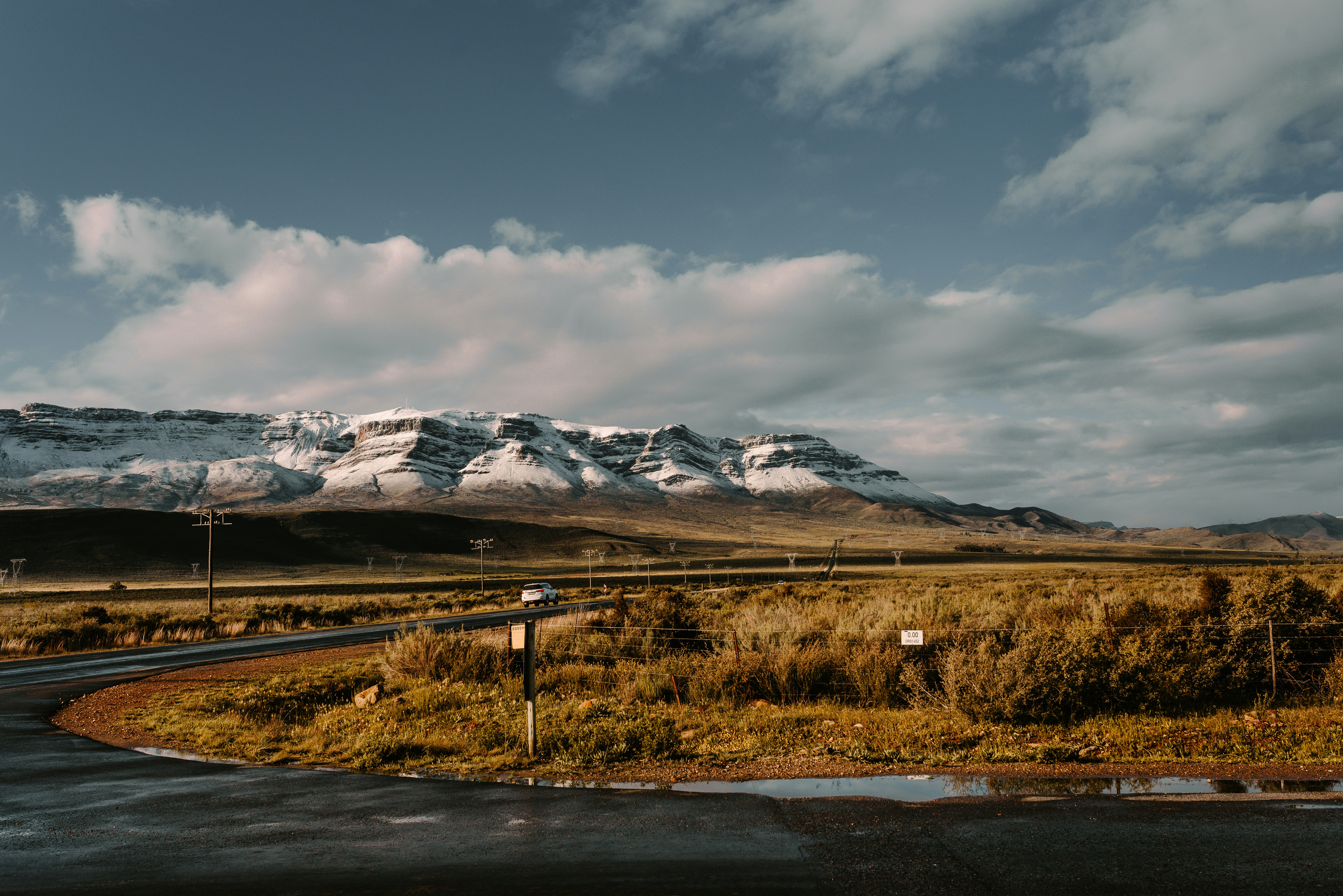 brown grass field near snow covered mountain under cloudy sky during daytime