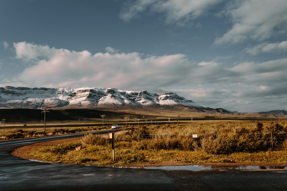 brown grass field near snow covered mountain under cloudy sky during daytime