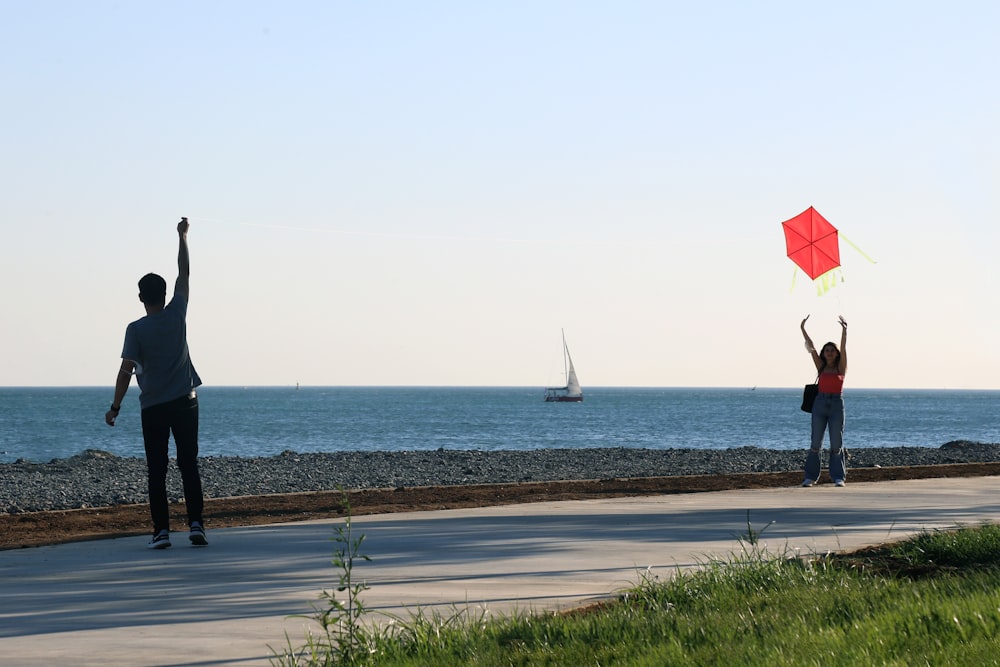 man in black jacket holding red umbrella standing on seashore during daytime