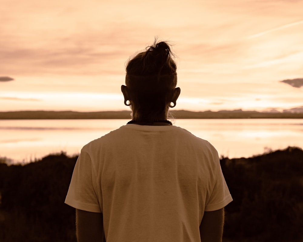 man in white crew neck t-shirt standing on hill during sunset