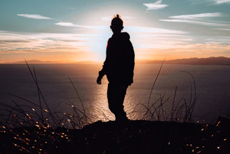 silhouette of man standing on hill during sunset