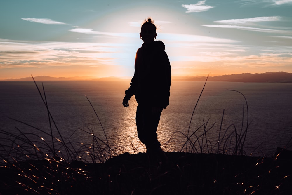 silhouette of man standing on hill during sunset