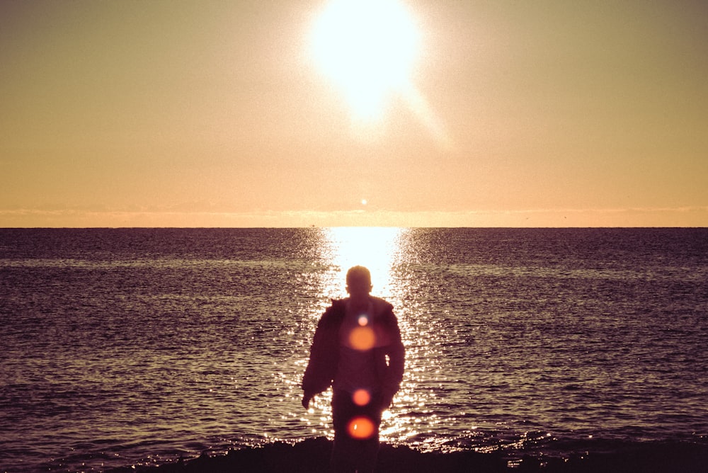 Hombre en traje de neopreno negro de pie en la orilla del mar durante la puesta del sol