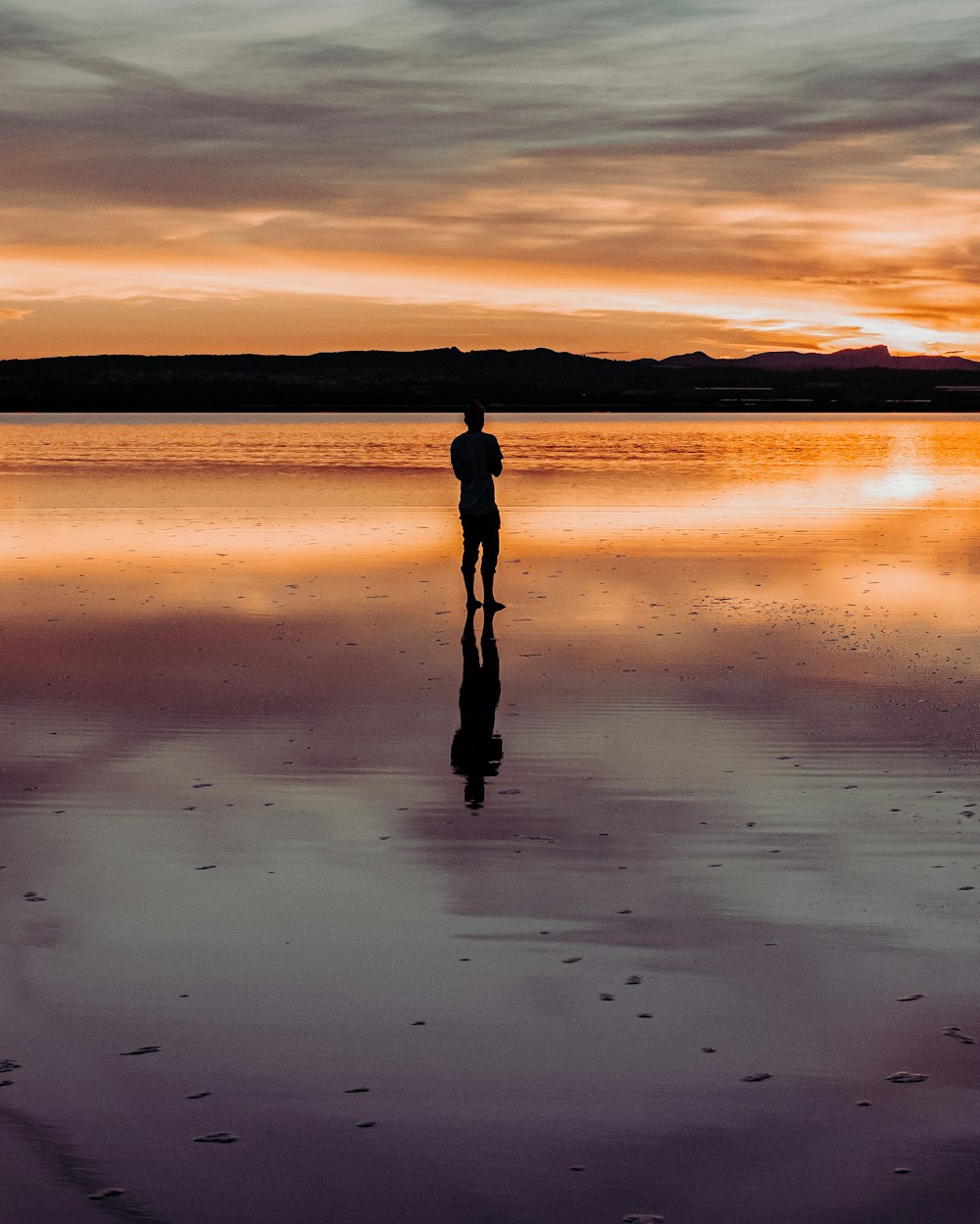 silhouette of person standing on water during sunset