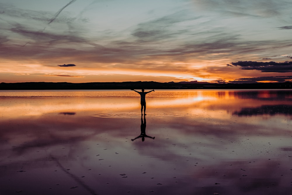 silhouette of man standing on body of water during sunset