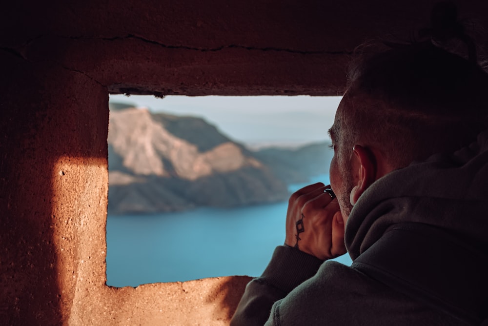 man in gray hoodie leaning on brown rock