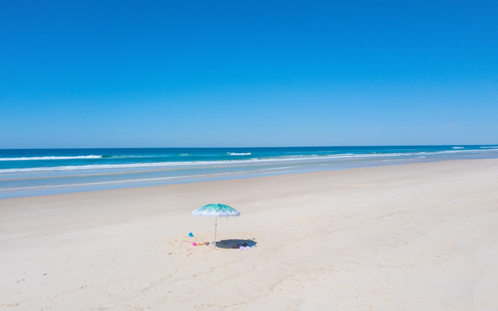 Persona que sostiene una sombrilla blanca caminando en la playa durante el día