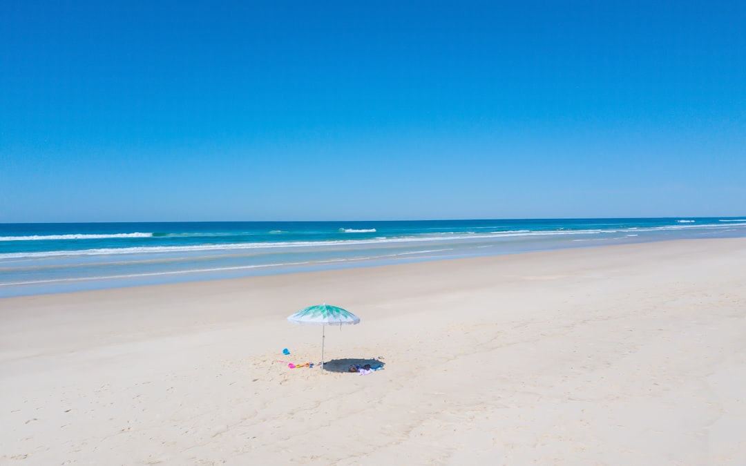 person holding white umbrella walking on beach during daytime