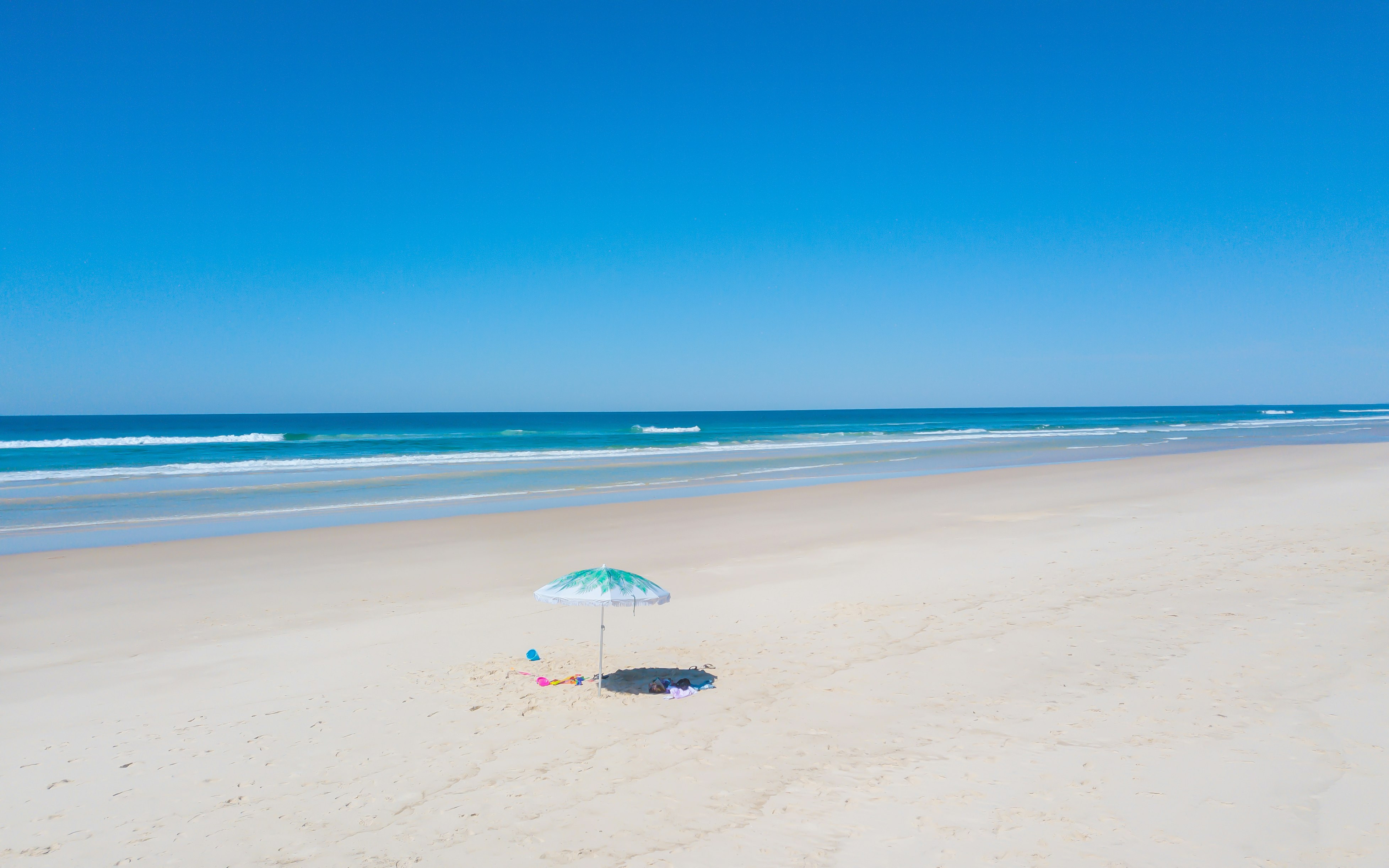 person holding white umbrella walking on beach during daytime