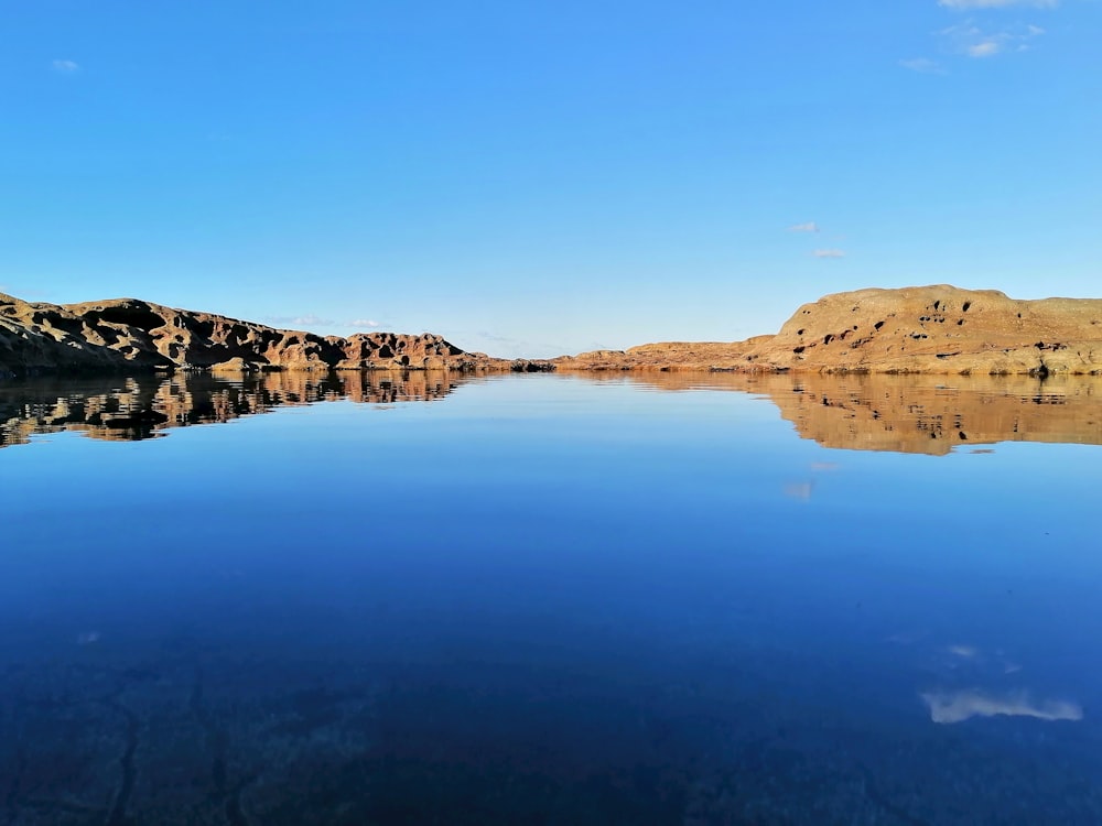 brown rocky mountain beside lake under blue sky during daytime