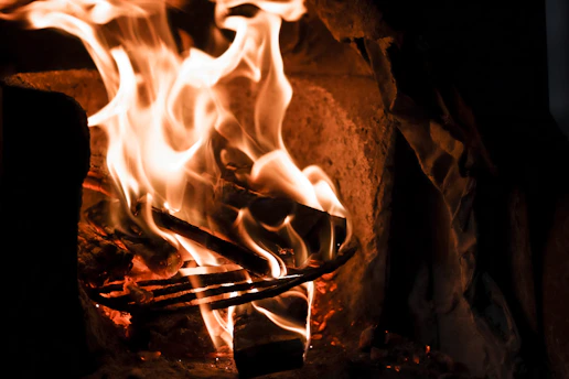 Golden amber flames dancing over a cozy fireplace inside Lakeside Ember cafe, with rustic wooden beams above.