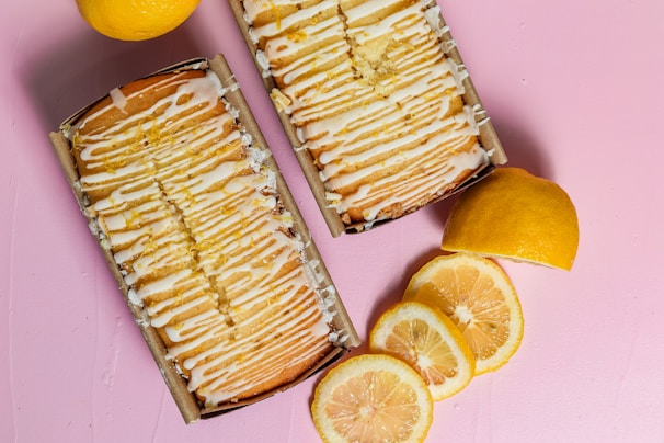 A vibrant lemon drizzle cake with a shiny glaze and lemon zest curls on top.