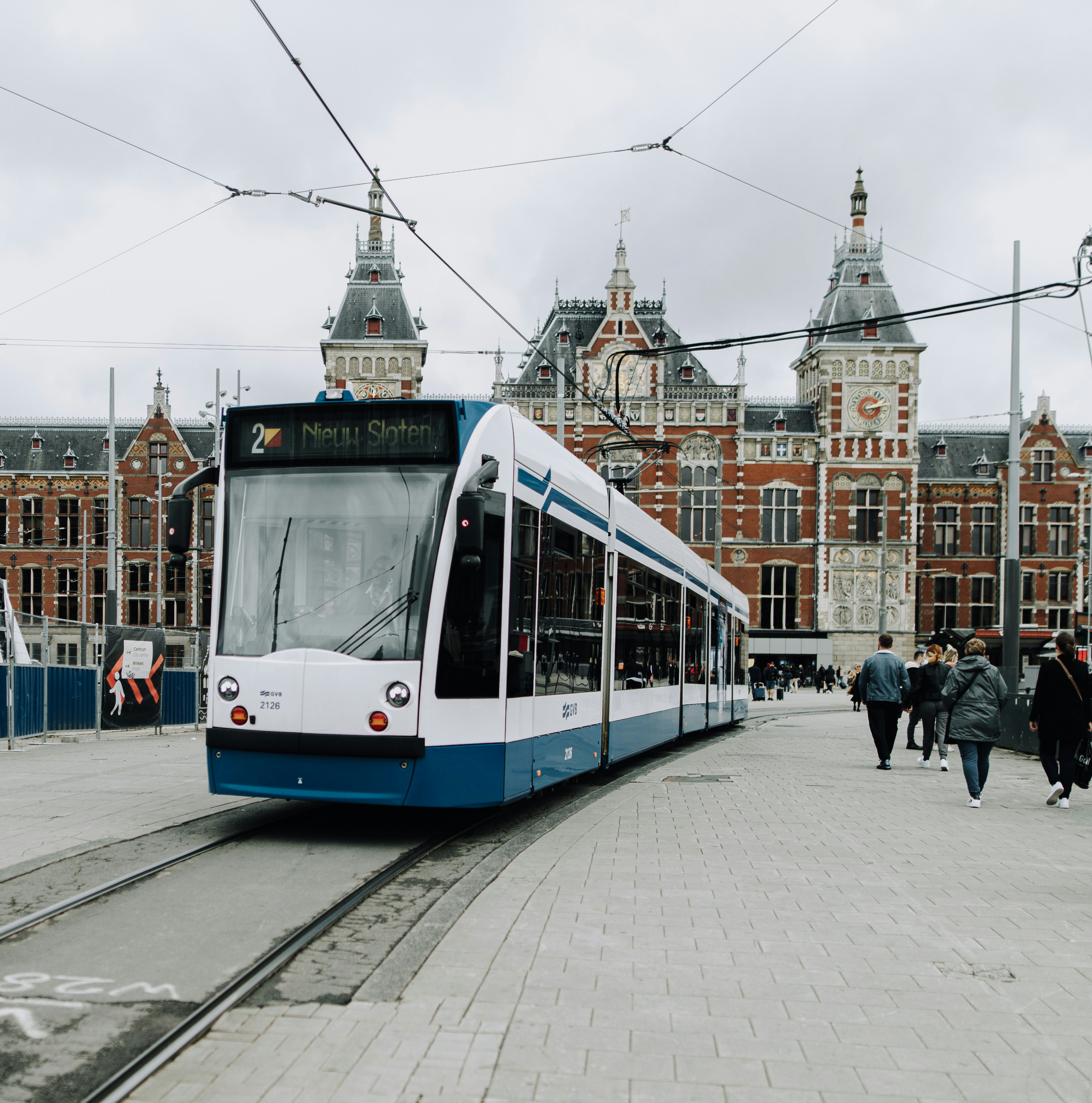 people walking on sidewalk near white and blue train during daytime