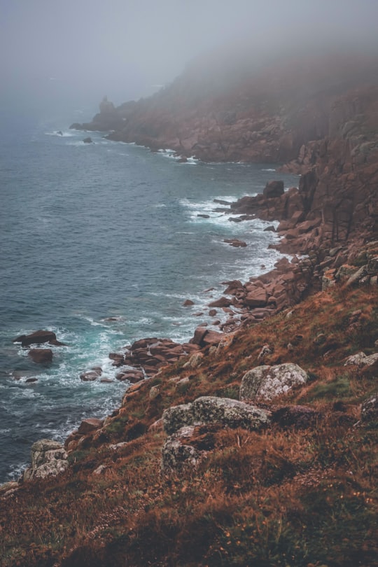 brown rocky mountain beside body of water during daytime in Land's End United Kingdom