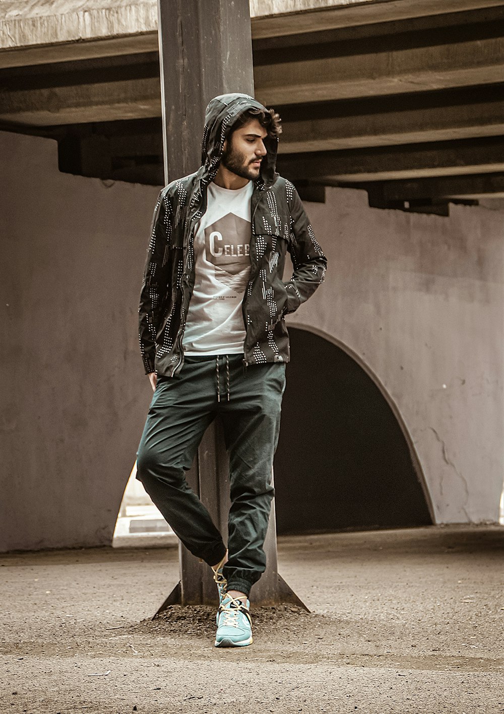 man in black leather jacket and blue denim jeans standing near brown wall during daytime