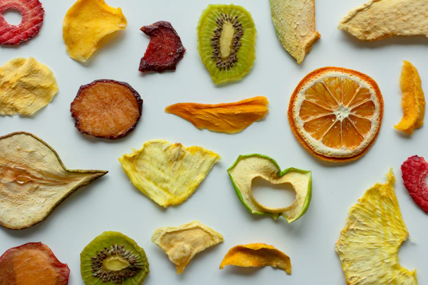 Overhead view of a vibrant assortment of freeze-dried fruits and snacks arranged in a spiral pattern with neon accents.